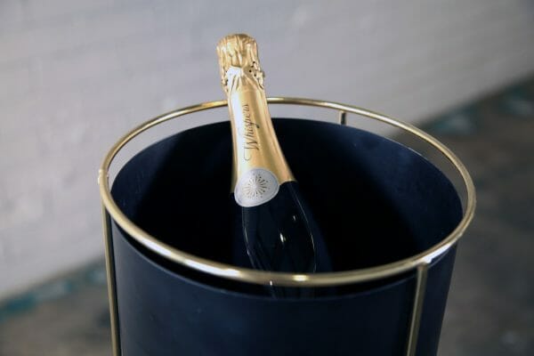 BLACK AND GOLD WINE BUCKET 03_resized A bottle of champagne displayed in a black bucket, featuring a refined gold stand for an elegant presentation at your wedding event.