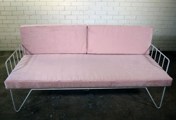 BLUSH PINK COUCH 01_resized A stylish blush pink velvet wire couch with metal legs against a white brick wall, perfect for events and available for hire in Perth.
