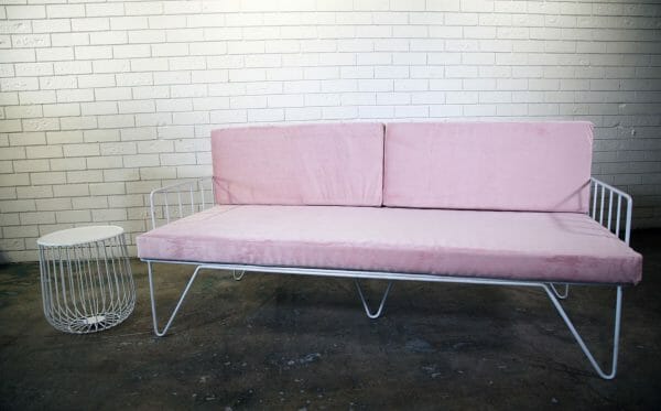 BLUSH PINK COUCH 02_resized A stylish blush pink velvet couch with white wire legs against a white brick wall, perfect for events and available for hire in Perth.
