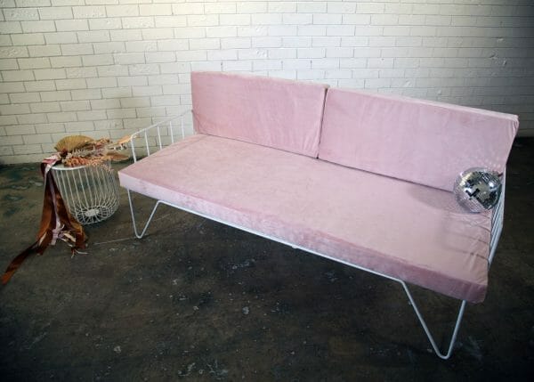 BLUSH PINK COUCH 03_resized A stylish blush pink couch with metal legs against a white brick wall, perfect for events and available for hire in Perth.