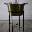 A stylish golden champagne bucket holds two bottles of champagne, elegantly displayed on a black stand for your next celebratory occasion.