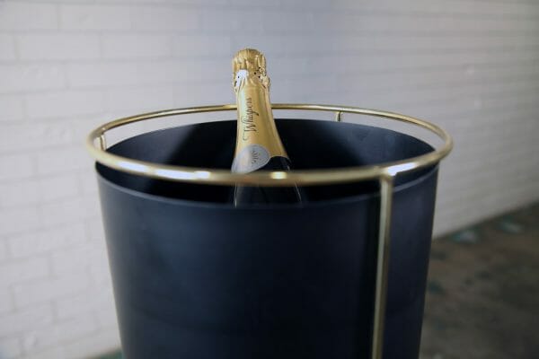 BLACK AND GOLD WINE BUCKET A bottle of champagne nestled in a black bucket, enhanced by a striking gold stand for a touch of luxury, a fantastic addition to your next party event.