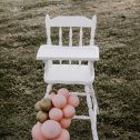 A white vintage high chair surrounded by pink and gold balloons, perfect for events, available for hire in Perth.