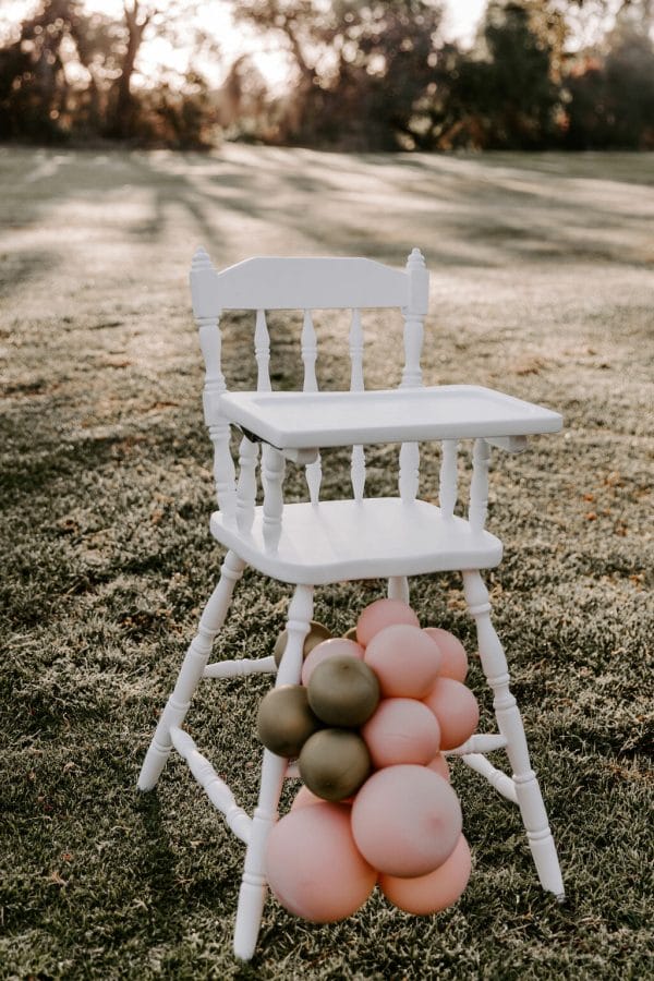 White-vintage-highchair-for-hire-kids-party-hire-fun-hq-Perth-wa Elegant white high chair with pink and gold balloons, a lovely addition for events, available for hire in Perth.