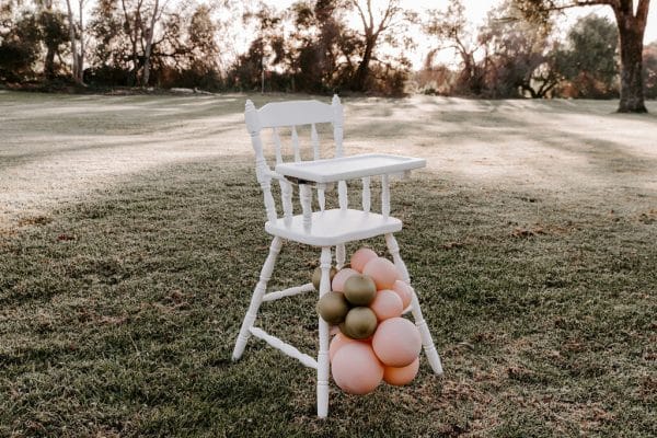 White-vintage-highchair-kids-party-hire-fun-hq-Perth Charming white high chair adorned with pink and gold balloons, ideal for events, offered by RSVP Event Hire in Perth.